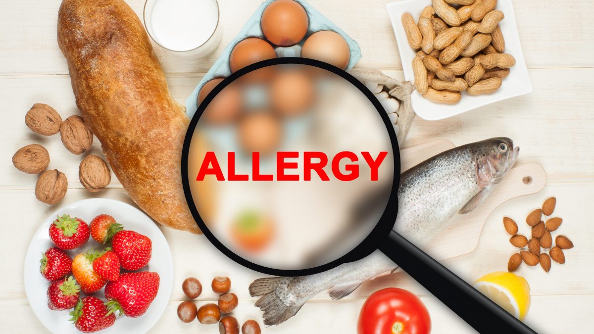 picture of various foods surrounding the word allergy in the middle being shown through a magnifying glass