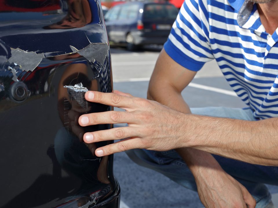 person's hand inspecting the damage from a parking lot car accident