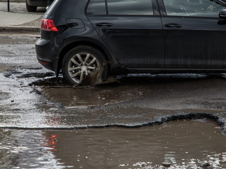rear of car driving through pothole filled with dirty water