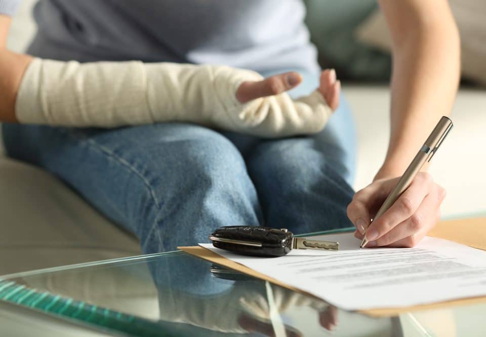 Woman with Broken Arm Is Signing Legal PAper Work On A Table With Car Keys