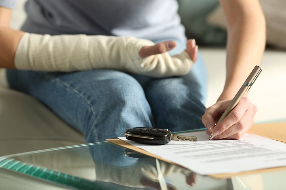 Woman with Broken Arm Is Signing Legal PAper Work On A Table With Car Keys