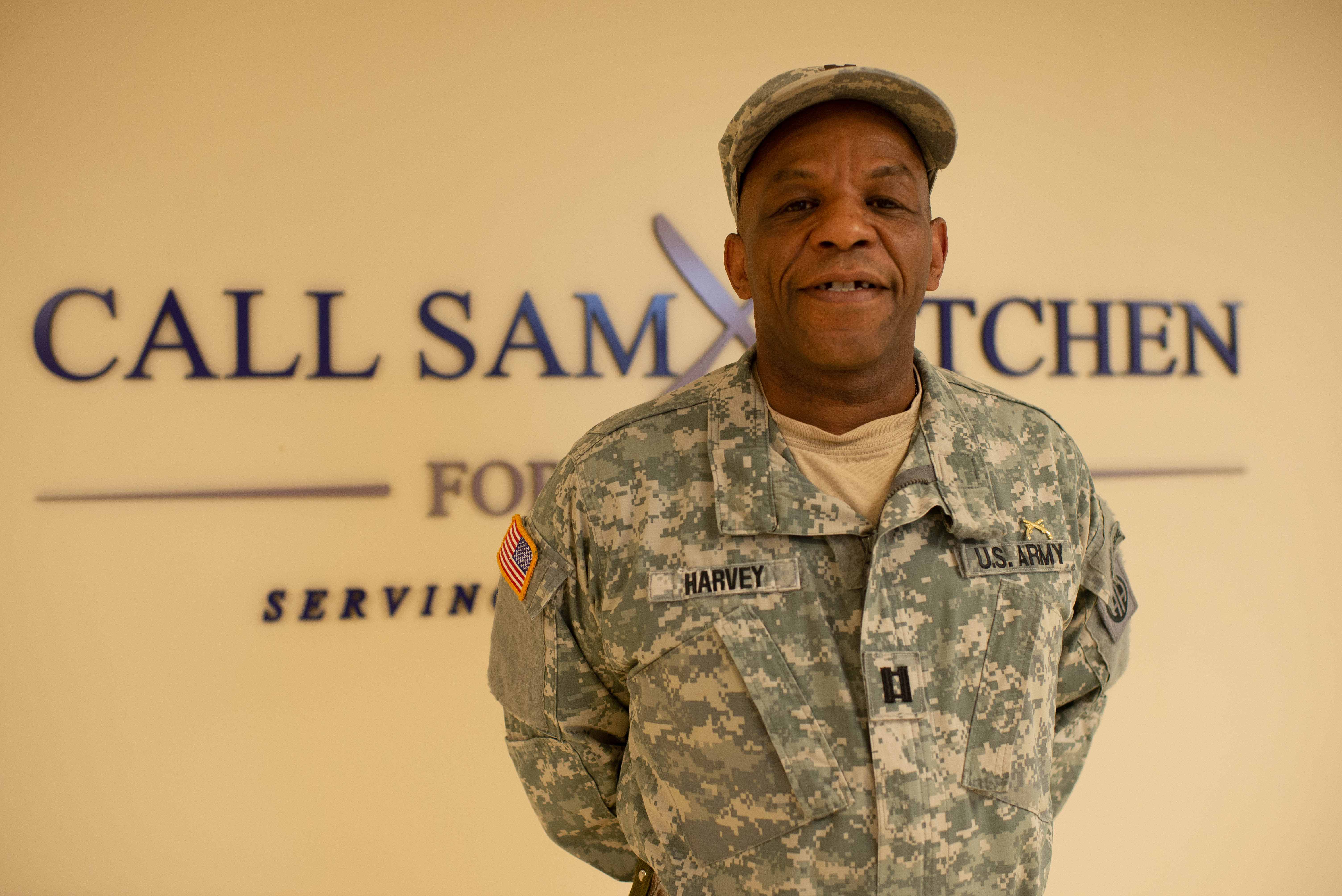 Military Veteran standing in uniform in front of the Call Sam Kitchen for Veterans Sign
