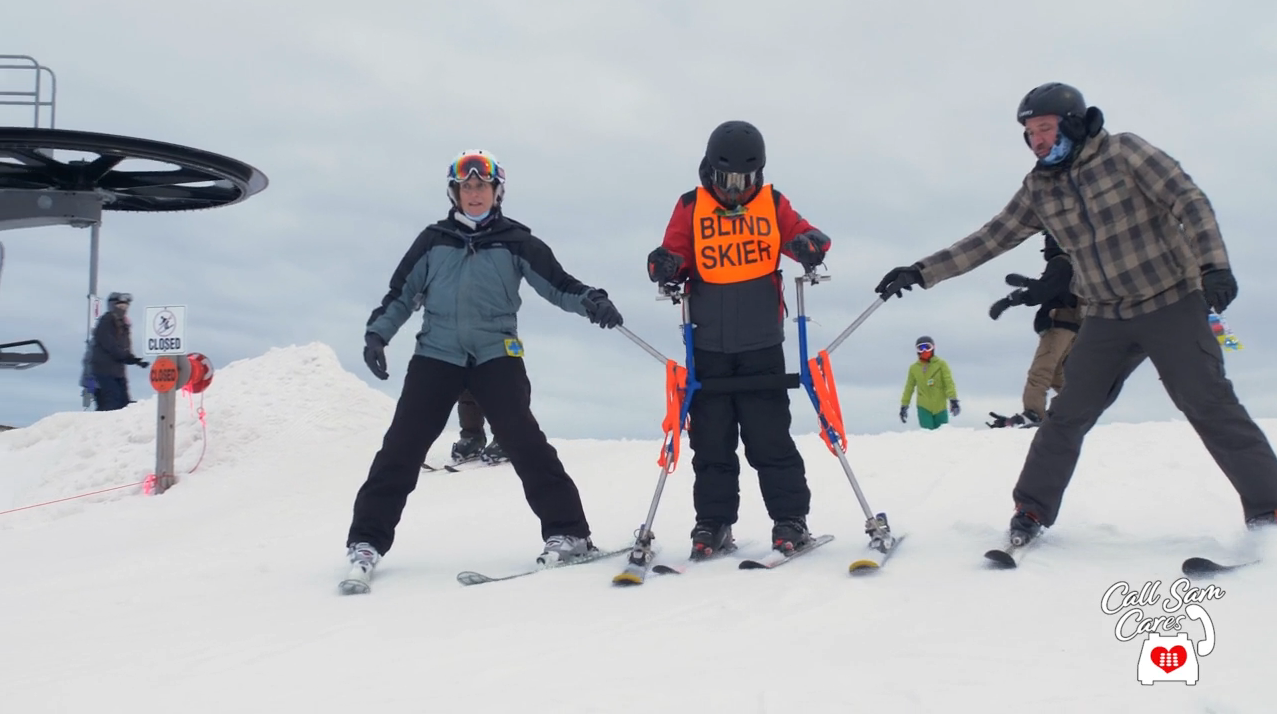 two people assisting a disabled person in skiing down a hill