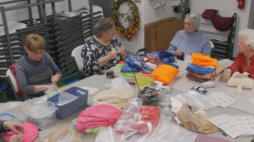 Volunteers at Knit Michigan sitting around a table knitting various items.