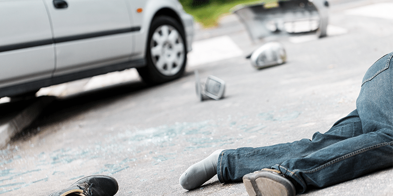 person laying on ground after being hit by car with glass everywhere on the ground