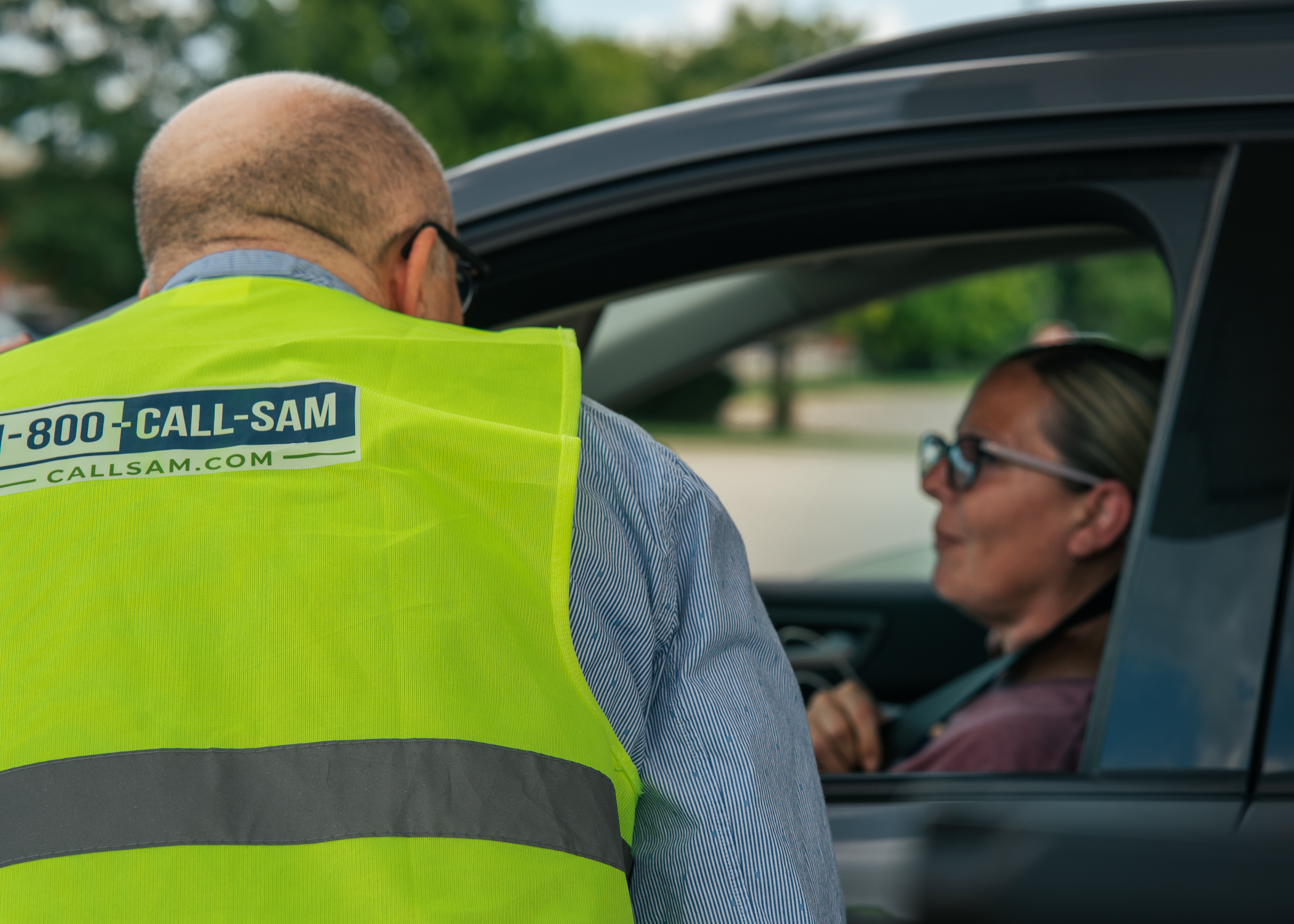 man standing outside of car talking to woman inside of car through driver side window