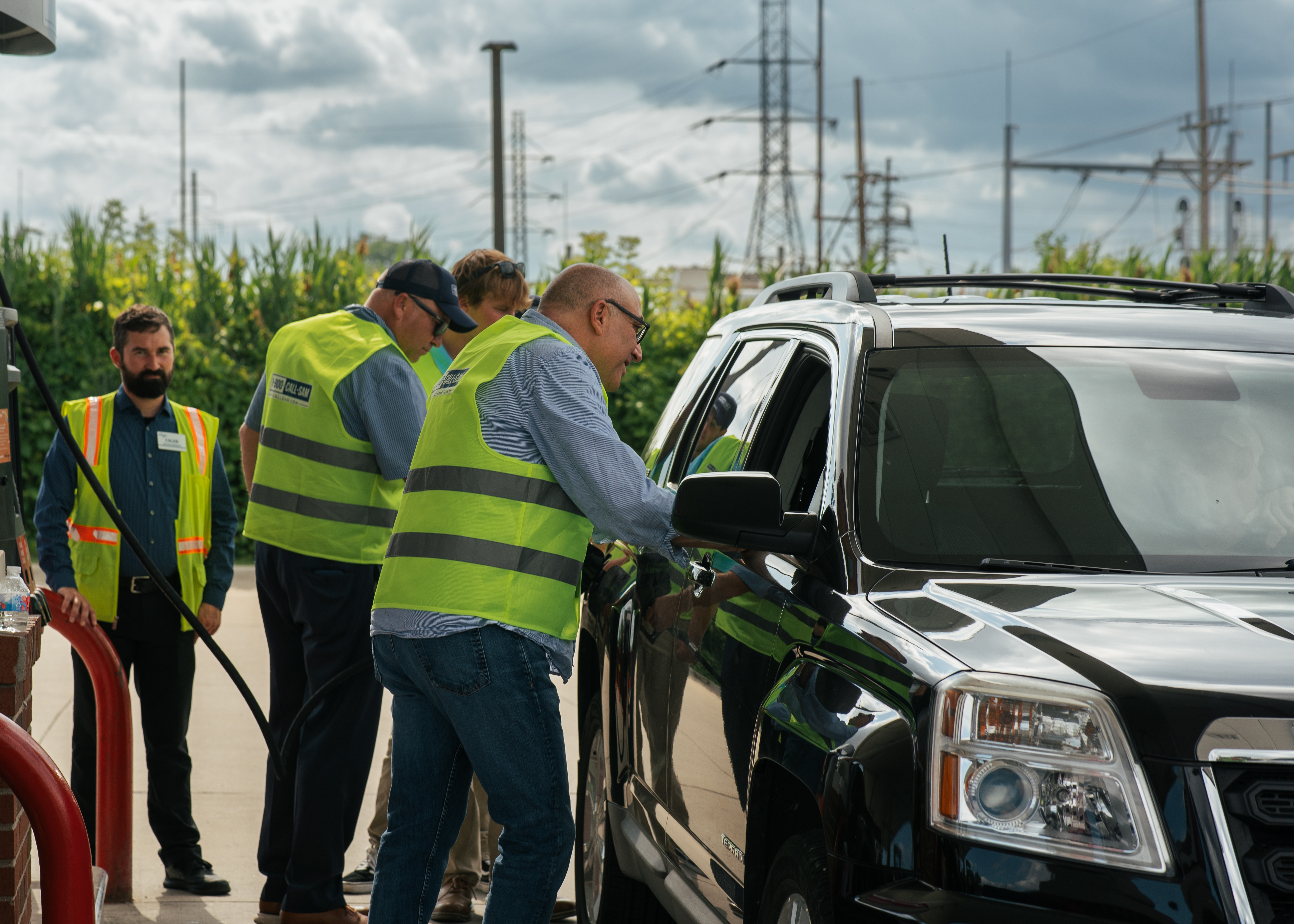 one person talking to someone inside a car through the passenger window while others stand next to same car