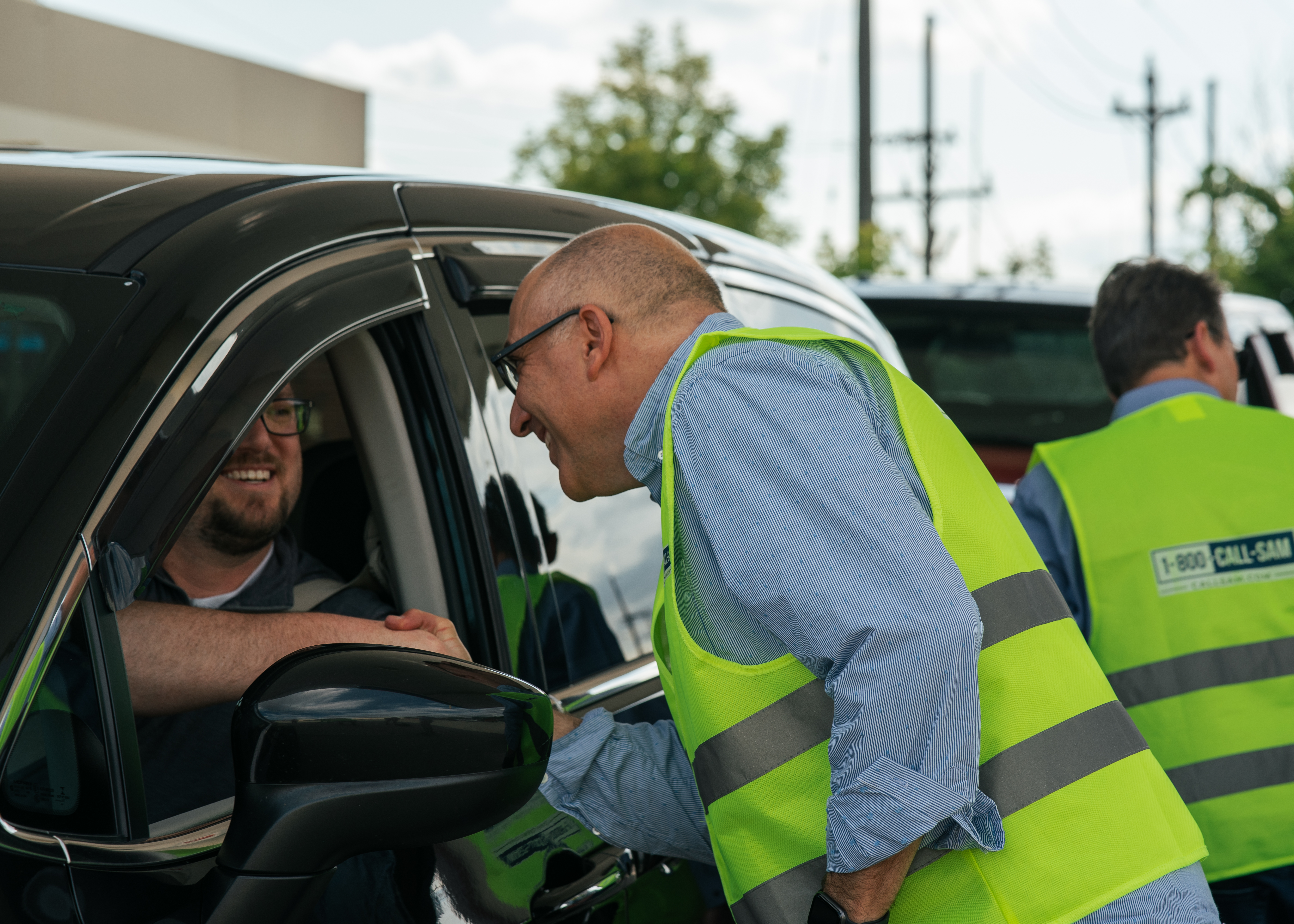 Man shaking hands with another man through the driver window of a car