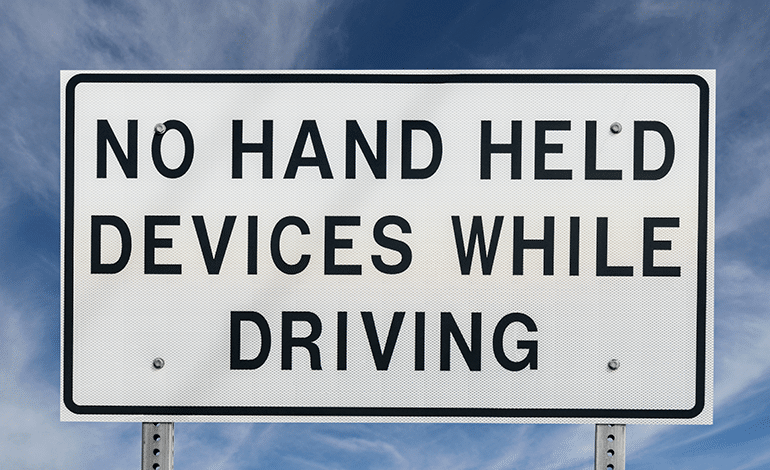 White Sign that says No Hand Held Devices While Driving in Black Letters