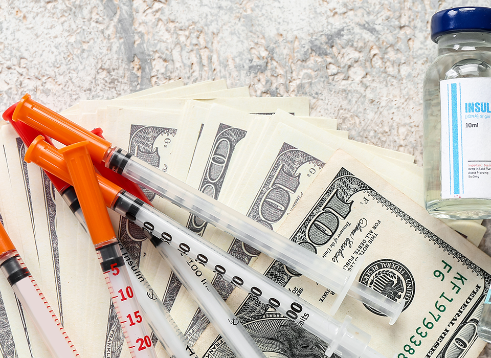 hypodermic syringe and insulin viles on top of one hundred dollar bills
