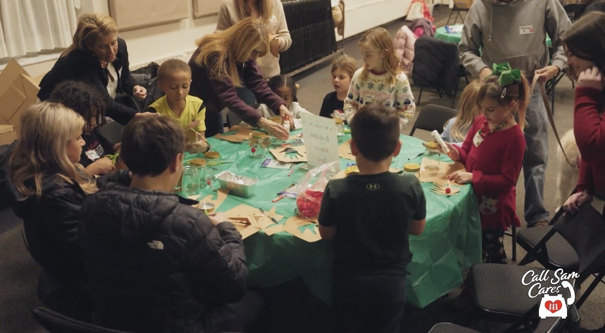 Children and adults gathered around a round table participating in a crafting activity.