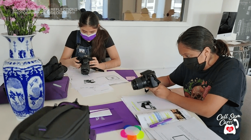 2 girls with cameras sitting at desk studying