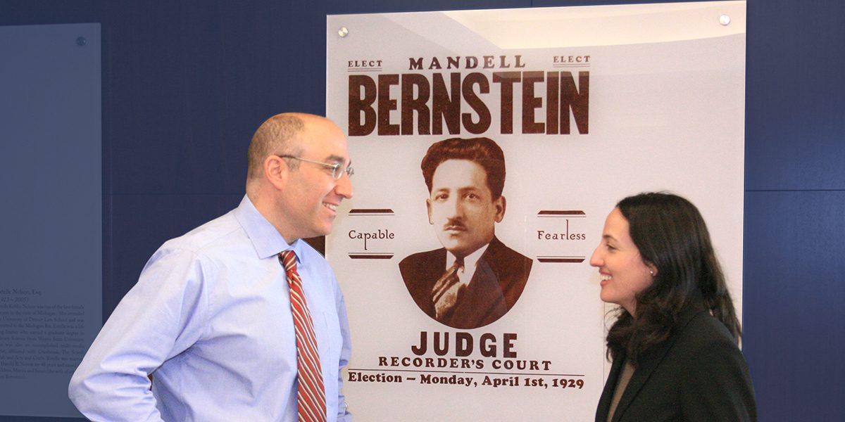 Mark Bernstein and Beth Bernstein Miller standing next to poster of Mandell Bernstein